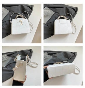 Detail view of white crocodile pattern handbag with gold hardware and deer charm