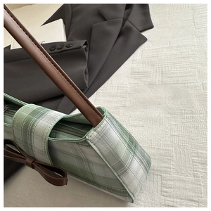 Detail of green and white plaid fabric underarm bag with brown leather bow and strap