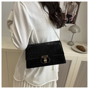 Close-up of black crocodile embossed shoulder bag featuring a gold T-shaped twist lock