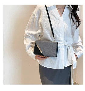 Detail view of stylish grey and black leather shoulder bag with gold metal trim