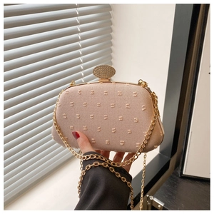 Detail of light pink clutch with textured dots, gold chain, and diamond oval clasp