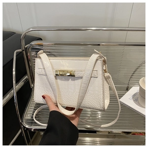 Detail of white crocodile pattern shoulder bag with golden lock and metal shelf background