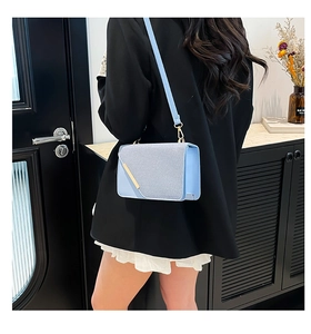 Light blue textured crossbody bag with gold metal bar accent on black suit