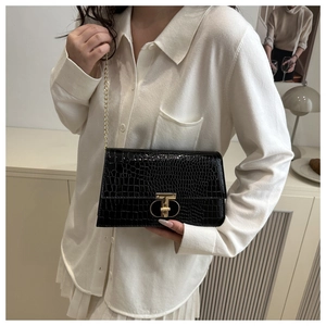 Detail of black faux crocodile leather bag with gold T-shaped lock and chain strap