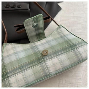 Detail view of the magnetic closure and woven green plaid fabric of the shoulder bag