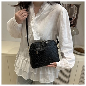 Détail du sac coquille tissé noir avec ferrures dorées porté avec un haut en dentelle