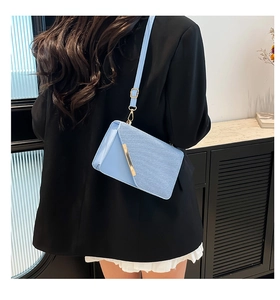 Detail shot of light blue crossbody bag with triangle flap and golden metal bar on model