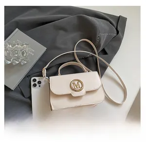 Detail of cream white mini crossbody bag with gold M buckle on grey blazer backdrop