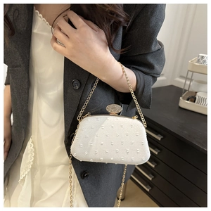 White textured shoulder bag with rhinestone buckle and gold chain on a model