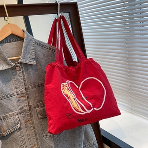 Red nylon tote bag with white apple print hanging next to a blue denim jacket