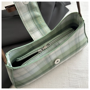 Detail of green plaid baguette bag showing top zipper closure and brown leather strap