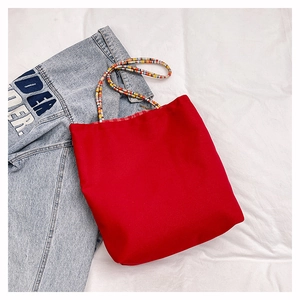 Detail of red fabric tote bag with colorful braided handles on denim background