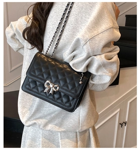 Detail of black quilted crossbody bag with silver bow clasp worn by a model