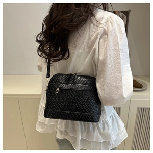 Détail d'un sac à bandoulière noir tressé avec finitions dorées porté par un mannequin