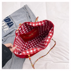 Detail of red tote bag with checkered lining and beaded strap on denim jacket
