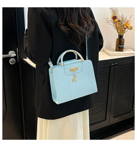 Detail of light blue crocodile-embossed leather bag with deer pendant and gold handle