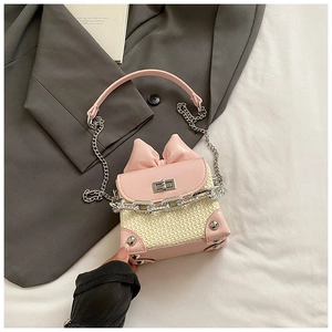 Close-up of pink bow and silver chain detail on a cream woven mini crossbody bag