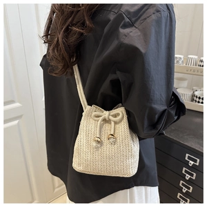 Detail of beige straw bucket bag featuring herringbone weave texture and drawstring bow