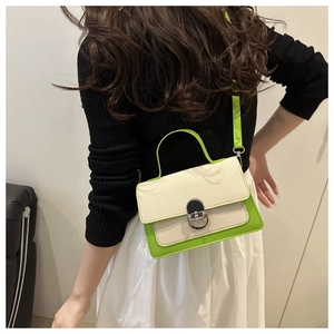 Detail shot of ivory and neon green color-block handbag worn with a chic outfit