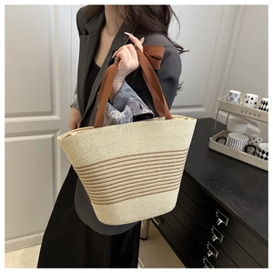 Straw tote bag with beige and brown stripes held by a model in a modern home setting
