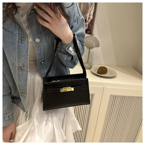 Detail of black crocodile texture shoulder bag with golden lock on a model outfit