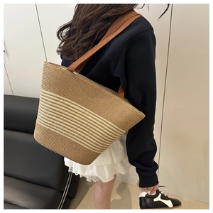 Detailed view of striped woven straw tote bag with brown fabric shoulder strap on model