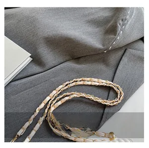 Detail of white leather shoulder strap woven with gold metal chain on grey blazer