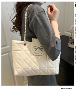 Detail of white quilted tote bag with silver bow clasp and metal chain shoulder strap