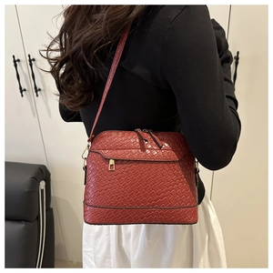 Detail of brick red woven crossbody bag with gold hardware shown on a model