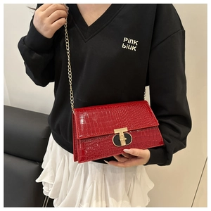 Detail view of red crocodile embossed chain bag with gold T-shaped clasp on a model