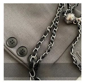 Détail de la boule métallique argentée et de la chaîne en cuir sur un sac bandoulière