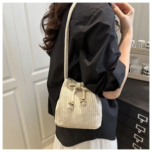 Detail of cream woven bucket bag with drawstring closure and metal bead accents