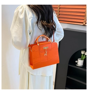 Detail view of bright orange crocodile texture handbag with gold handle and deer charm