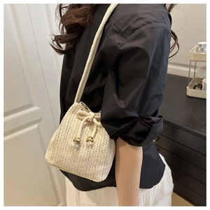 Detail of hand-woven off-white bucket bag with wave texture and gold ball drawstring