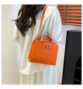 Detail of orange embossed crossbody bag with gold handle and deer charm on model