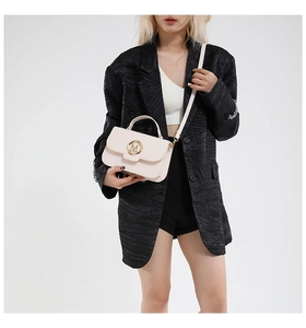 Detail of beige leather crossbody bag with golden M-letter buckle on black blazer
