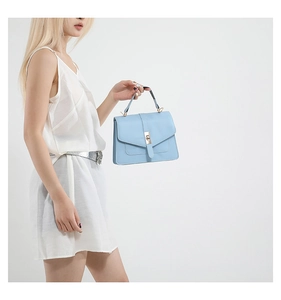 Bolso de mano azul claro minimalista con cierre dorado sobre un vestido blanco