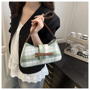 Detail of green plaid baguette bag featuring a leather bow and slim shoulder strap