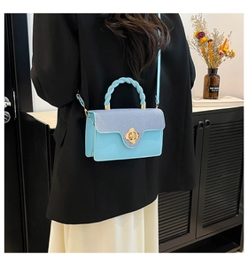 Detail of light blue denim flap bag featuring a golden flower clasp and woven handle