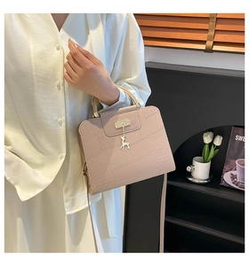 Close-up of pink crocodile pattern handbag with golden deer charm and metal handle