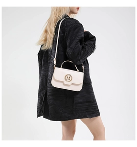 Modern off-white leather shoulder bag with gold M-logo and adjustable strap on a model