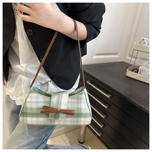 Close-up of green checkered underarm bag with leather bow and slim brown shoulder strap
