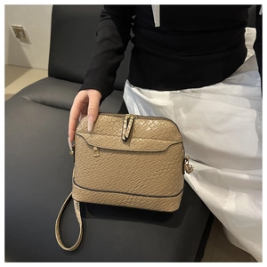 Close-up of beige shell crossbody bag with crocodile texture and double zipper detail
