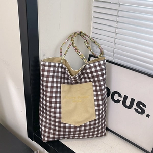 Plaid canvas tote bag with woven beaded handle and front pocket shown in a lifestyle setting