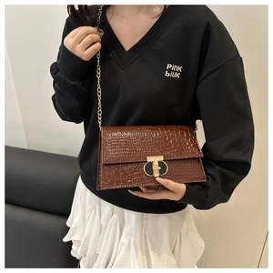 Close-up of brown croc-effect leather texture with golden T-bar metal lock on crossbody bag