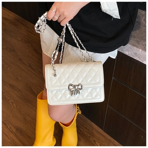 Detail of white quilted crossbody bag featuring silver bow clasp and chain strap