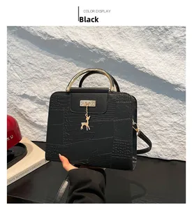 Detail of black faux leather handbag with crocodile texture and gold deer pendant