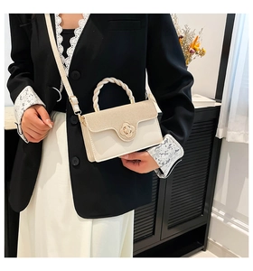 Detail of cream crossbody bag with woven handle and gold clover clasp on a model