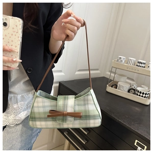Detail of green and white plaid shoulder bag with brown leather bow and fabric texture