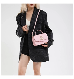 Detail of pink crossbody bag with gold M-logo clasp paired with a black blazer suit